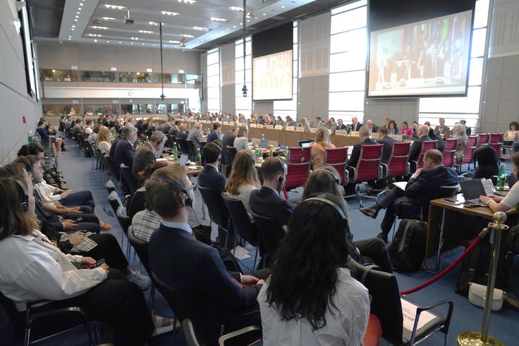 Large conference room filled with seated attendees, facing a presentation screen.