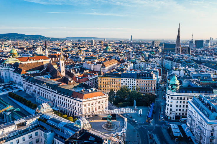 Aerial view of a European cityscape with historic buildings, a tall spire, and a clear blue sky.