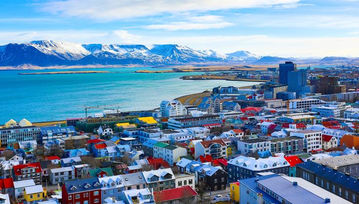 Colorful Reykjavik buildings, with a coastal view and snow-capped mountains in the background.
