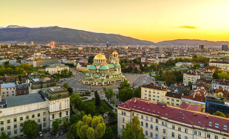 Aerial view of Sofia at sunset, with Alexander Nevsky Cathedral and mountain backdrop.