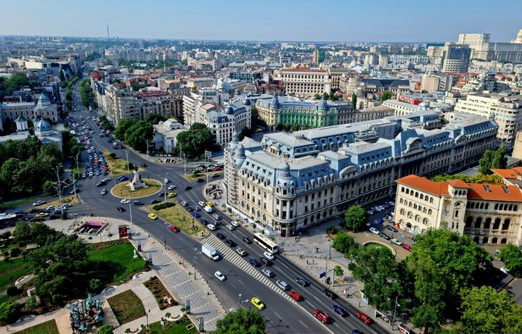 Aerial view of a busy city with classic architecture, green spaces, and a roundabout.