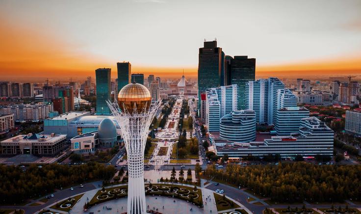 City skyline at sunset with a tall tower and modern buildings, featuring a golden sphere at the top.