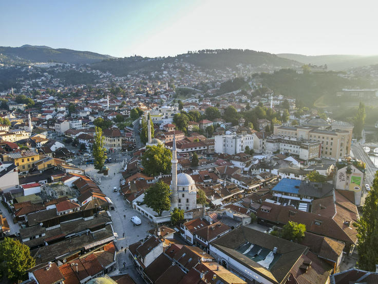 Aerial view of a town with a mosque, surrounded by hills and buildings, under a clear sky.