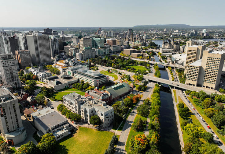 Aerial view of a city with modern buildings, a river, and tree-lined streets on a clear day.