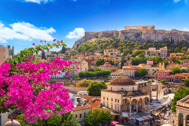 Athens cityscape with vibrant pink flowers, historic buildings, and the Acropolis perched on a hill under a clear blue sky.