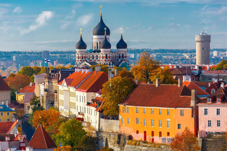 Old town with colorful rooftops, a cathedral with onion domes, and autumn trees under a clear sky.