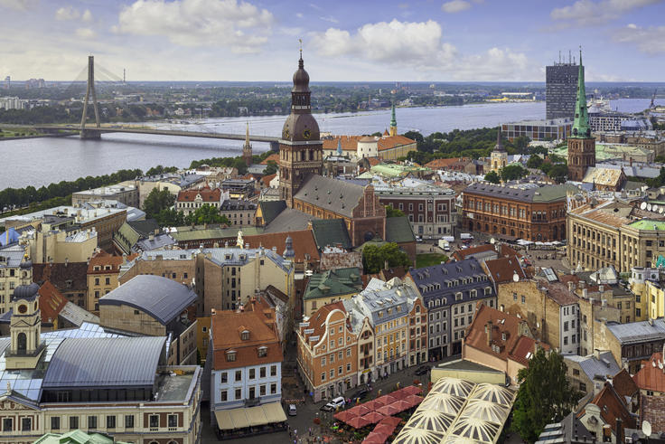 Aerial view of a European city with colorful buildings, a river, and a distant bridge under a blue sky.
