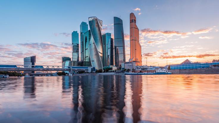 Moscow, Russian Federation: Skyscrapers reflecting in a river at sunset, with a vibrant sky.