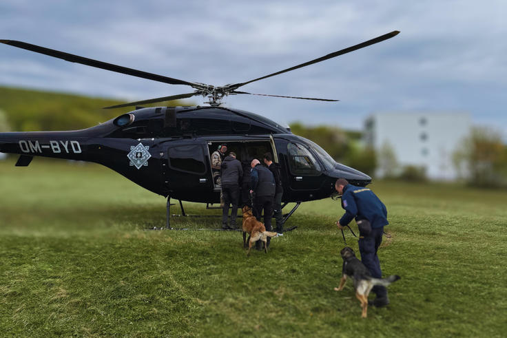 Police officers boarding a black helicopter with two German Shepherds on a grassy field.