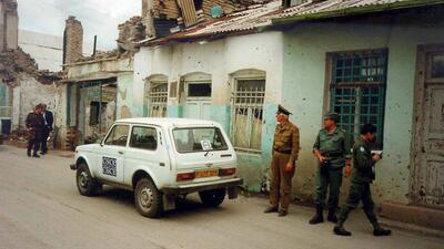 OSCE vehicle and military personnel next to damaged buildings.