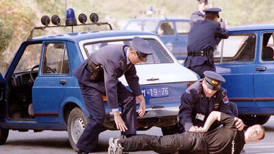Police officers detaining a person on the ground next to blue police cars.