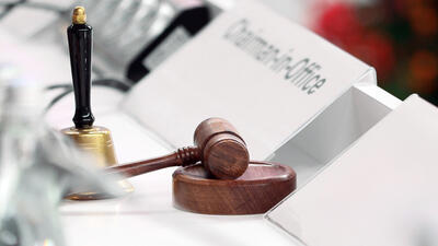 A bell, a gavel and a sign reading Chairman-in-Office on a white conference table.