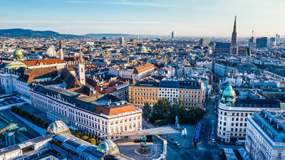 Aerial view of a European cityscape with historic buildings, a tall spire, and a clear blue sky.