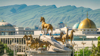 Golden horse statues on a rooftop with a cityscape and mountains in the background.