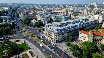 Aerial view of a busy city with classic architecture, green spaces, and a roundabout.