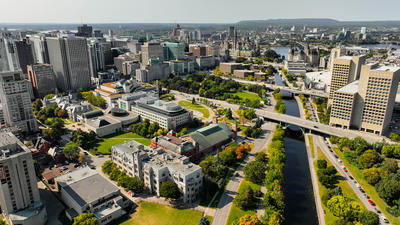 Aerial view of a city with modern buildings, a river, and tree-lined streets on a clear day.