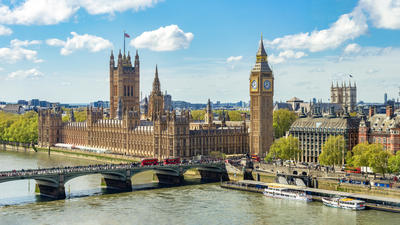 London's Houses of Parliament and Big Ben by the River Thames under a bright blue sky.