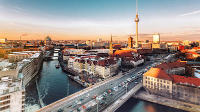 Aerial view of a cityscape at sunset with a river, bridges, and a tall TV tower in the distance.