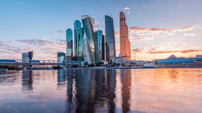 Moscow, Russian Federation: Skyscrapers reflecting in a river at sunset, with a vibrant sky.