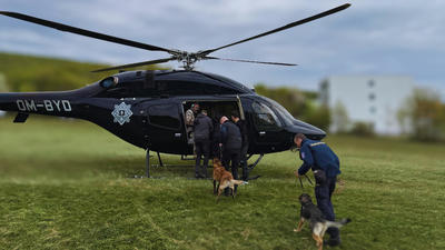Police officers boarding a black helicopter with two German Shepherds on a grassy field.