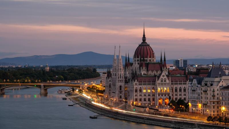 Hungarian Parliament Building by the river at dusk, with a glowing pink and orange sky.