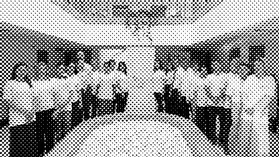 A group of people wearing white shirts stand in a semicircle around a stone-filled fountain, posing indoors beside a banner about activism against gender-based violence.
